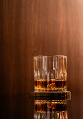 Glass of liquor scotch whiskey and ice cubes on wooden background and reflective table top. Space for text