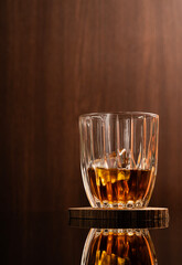 Glass of liquor scotch whiskey and ice cubes on wooden background and reflective table top. Space for text