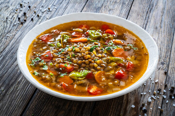 Fresh vegetable soup with lentil served in white bowl on wooden table
