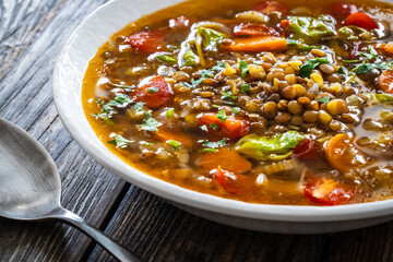 Fresh vegetable soup with lentil served in white bowl on wooden table
