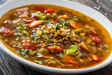 Fresh vegetable soup with lentil served in white bowl on wooden table
