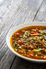 Fresh vegetable soup with lentil served in white bowl on wooden table
