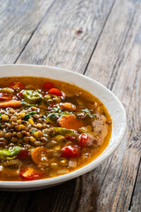 Fresh vegetable soup with lentil served in white bowl on wooden table
