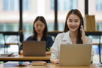 A woman is talking on her cell phone while sitting at a desk with a laptop.