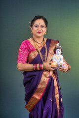 Traditional Indian woman wearing saree posing with God Lord Krishna idol