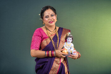 Traditional Indian woman wearing saree posing with God Lord Krishna idol