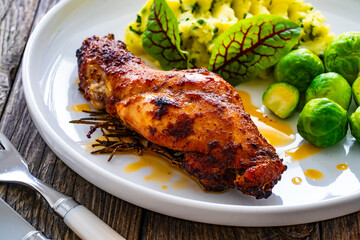 Roast rabbit thigh with mashed potatoes and boiled brussels sprouts served on white plate on wooden background
