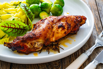 Roast rabbit thigh with mashed potatoes and boiled brussels sprouts served on white plate on wooden...