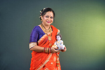 Traditional Indian woman wearing saree posing with God Lord Krishna idol