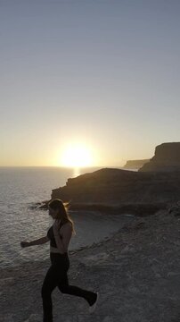 Video de dron con chica guapa en un atardecer con rocas grandes, en un barranco acantilado con el sol poniendose en una bella tarde de las islas canarias en un paraje natural de gran canaria.
