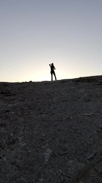 Video de dron con chica guapa en un atardecer con rocas grandes, en un barranco acantilado con el sol poniendose en una bella tarde de las islas canarias en un paraje natural de gran canaria.