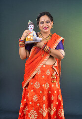 Traditional Indian woman wearing saree posing with God Lord Krishna idol