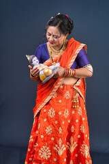 Traditional Indian woman wearing saree posing with God Lord Krishna idol
