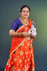 Traditional Indian woman wearing saree posing with God Lord Krishna idol