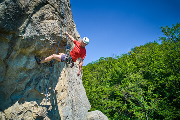 Aerial view of male rock climber ascending rugged limestone cliff with harness and rope for safety....