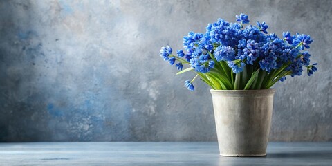 Floral arrangement of blue flowers in a grey vase with blurred empty space on the left