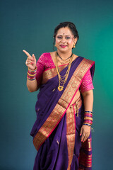 A successful cheerful traditional Indian woman pointing and presenting something with a hand or...