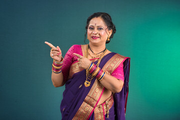 A successful cheerful traditional Indian woman pointing and presenting something with a hand or...