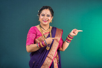 A successful cheerful traditional Indian woman pointing and presenting something with a hand or...