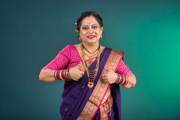 A successful cheerful traditional Indian woman pointing and presenting something with a hand or...