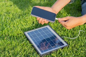 Shot view of man's hnads charging smartphone with solar panel on a lawn in a sunny summer day