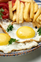 Breakfast plate with fried eggs, sausage, tomatoes, and fries served on a decorative blue plate