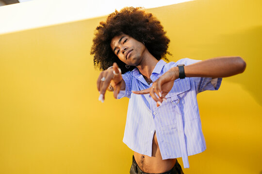 Gay man with curly hair gesturing near yellow wall