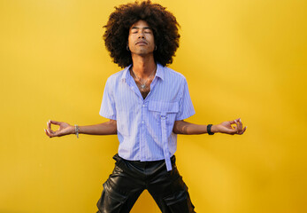 Young man meditating with eyes closed near yellow wall