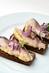 Open-faced sandwiches with herring and onions served on a white plate