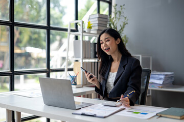 A woman is sitting at a desk with a laptop and a cell phone