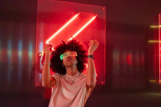 Young man wearing illuminated smart glasses and dancing near wall