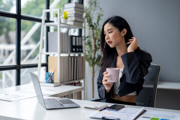 A woman in a business suit is sitting at a desk with a laptop