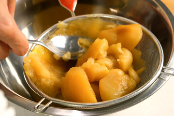 Woman hands cooking rubbing baked apples through sieve preparing fruit puree on kitchen. Culinary cuisine, healthy eating, baking concept. Prepare homemade marshmallows dish from apples, recipe.