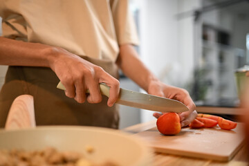 Close up image of man cutting tomatoes on a wooden cutting board, preparing healthy meal in kitchen