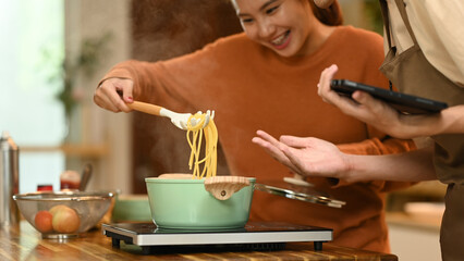 Cheerful young couple making delicious pasta in the kitchen