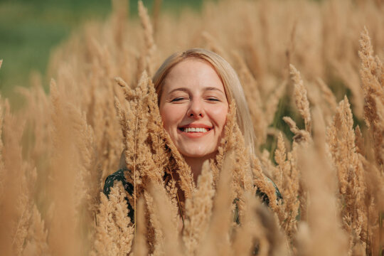 Smiling blond woman with eyes closed surrounded by reeds