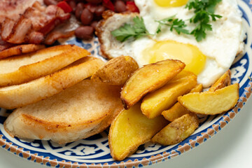Delicious breakfast plate featuring eggs, beans, bacon, and potato wedges served on a decorative dish
