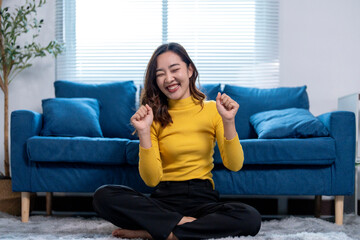 Obraz premium Happy young woman celebrating success while sitting on floor at home