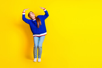 Photo of red hair model young cheerful woman in blue stylish pullover and jeans trying resist herself isolated on yellow color background