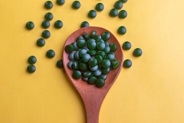 Top down picture of Green biotin tablets on a brown wood spoon kept on a yellow background