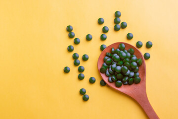 Green biotin tablets on a brown wood spoon kept on a yellow background