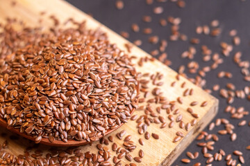 extreme closeup of healthy flax seeds scattered on a wooden spoon kept on the chopping board with a dark background 