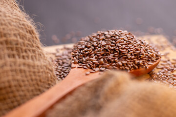 extreme closeup of healthy flax seeds scattered on a wooden spoon kept on the chopping board with a dark background 