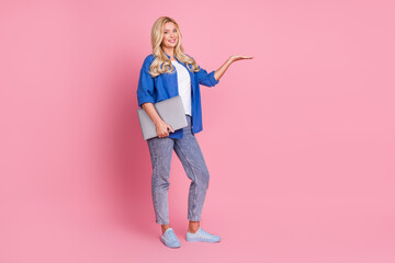 Full length photo of adorable lovely woman wear blue shirt holding modern gadget showing arm empty space isolated pink color background