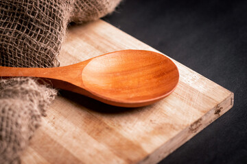 Extreme closeup of a big wooden spoon kept on a clopping board with a brown rug 
