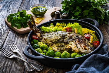 Roasted sea bream, boiled potatoes and brussels sprouts served in black dish on wooden table 