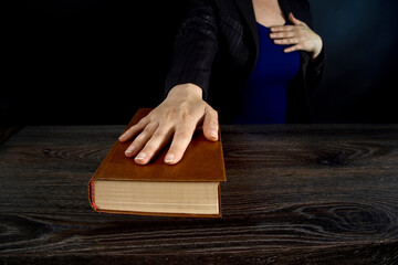 Female hand on the Bible and on the constitution book during the inauguration in parliament or the oath in court. Woman taking Oath of Office. Dark background, blue office clothes.