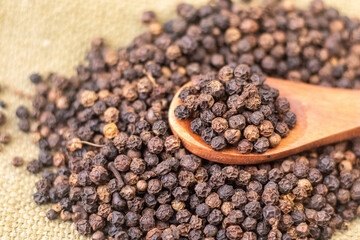 Closeup of black pepper on a wooden spoon with brown background with black pepper scattered 