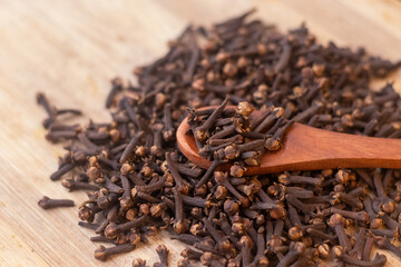 A close-up image of a pile of dried cloves on a wooden spoon. The cloves are a dark brown color and have a distinct, knobby shape. They are clustered together, showing their intricate textures