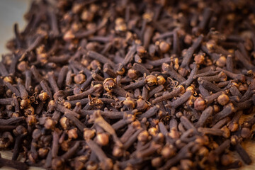 A close-up image of a pile of dried cloves. The cloves are a dark brown color and have a distinct, knobby shape. They are clustered together, showing their intricate textures